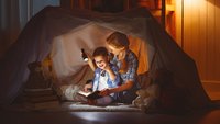 Mutter und Kind lesen im Licht von Taschenlampen unter einer Zeltplane, Foto stock.adobe.com © JenkoAtaman